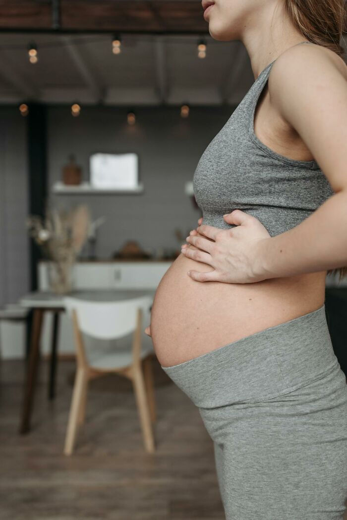 Pregnant woman holding her belly in grey workout clothes indoors