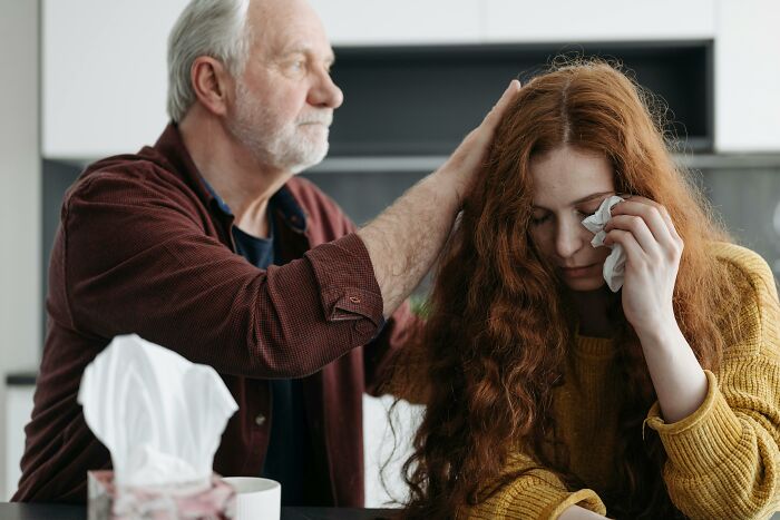 An older man comforts a crying woman with red hair, who is holding a tissue. Illustrates creepy experiences.