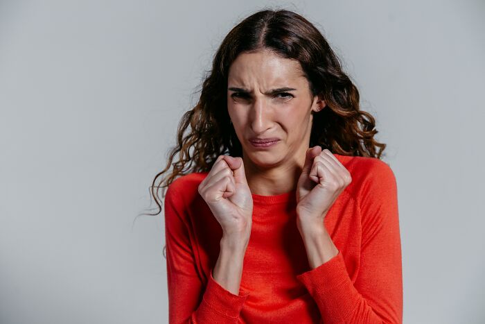A young woman with curly brown hair wearing a red shirt, looking confused and disgusted. Older generations may not understand Gen Z.