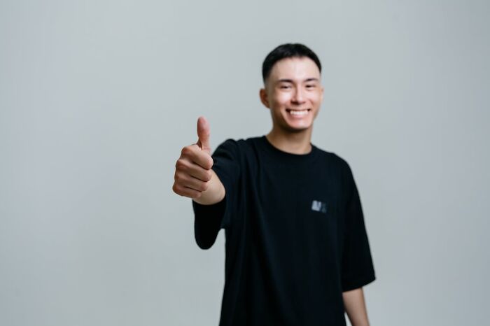 Smiling young man giving thumbs up wearing black t-shirt
