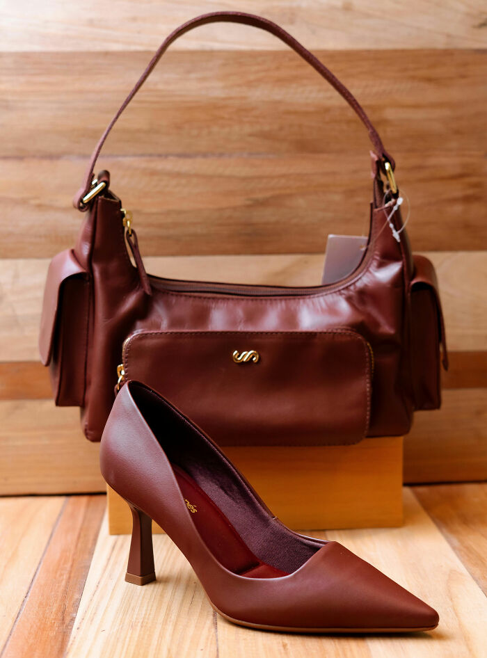 A brown leather handbag and a matching high heel shoe on a wooden surface, highlighting habits that save money.