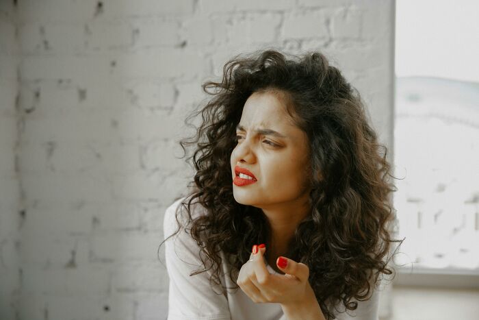 Frustrated woman with curly hair sitting near white brick wall