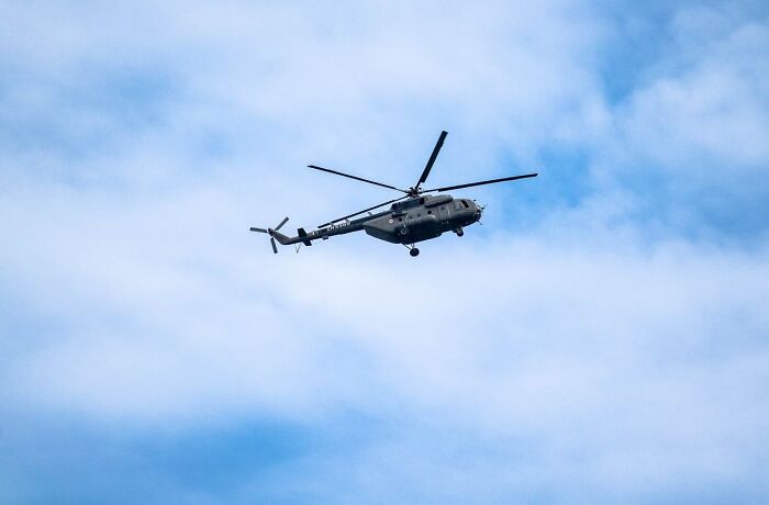 Military helicopter flying in blue sky with scattered clouds