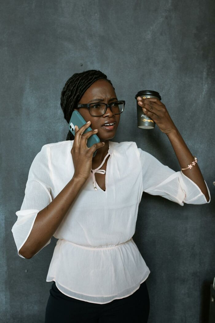 Woman talking on phone holding up a paper coffee cup looking frustrated