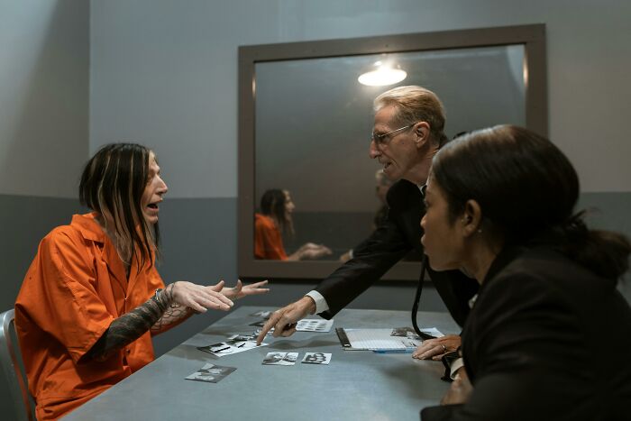 Lawyers discuss a difficult case with a client in an interrogation room. Defending hard cases.
