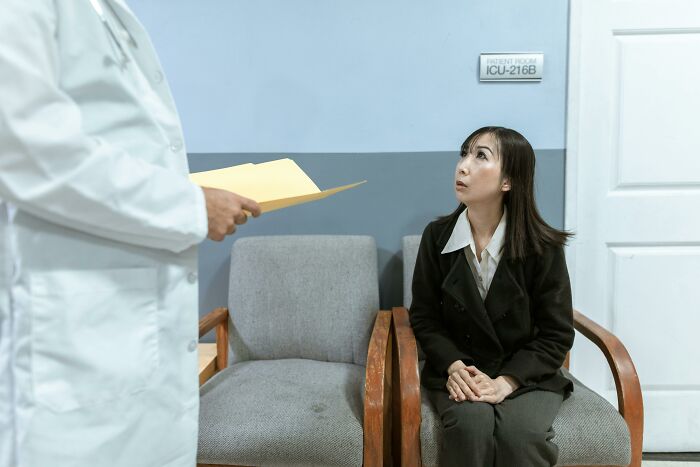 A doctor with a file talks to a worried woman in a waiting room; a creepy things scenario experienced.