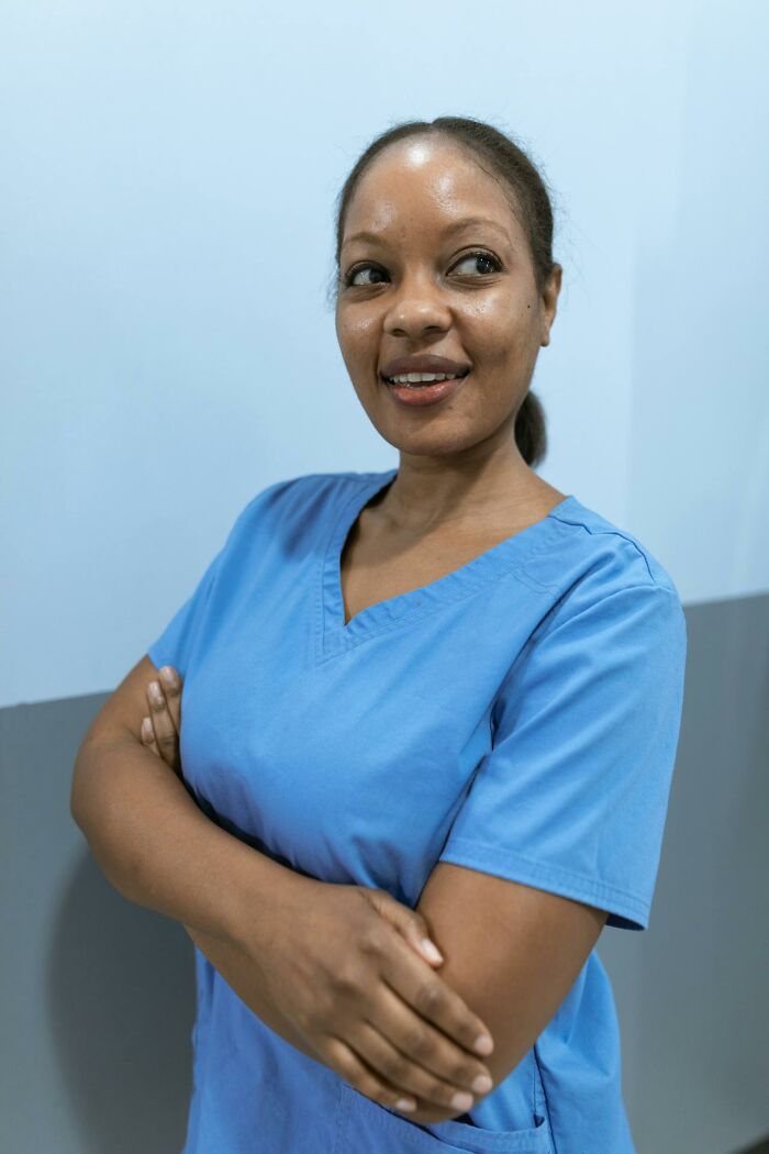 A female nurse in blue scrubs, arms crossed, smiles and looks right. Question reality with Matrix glitches.
