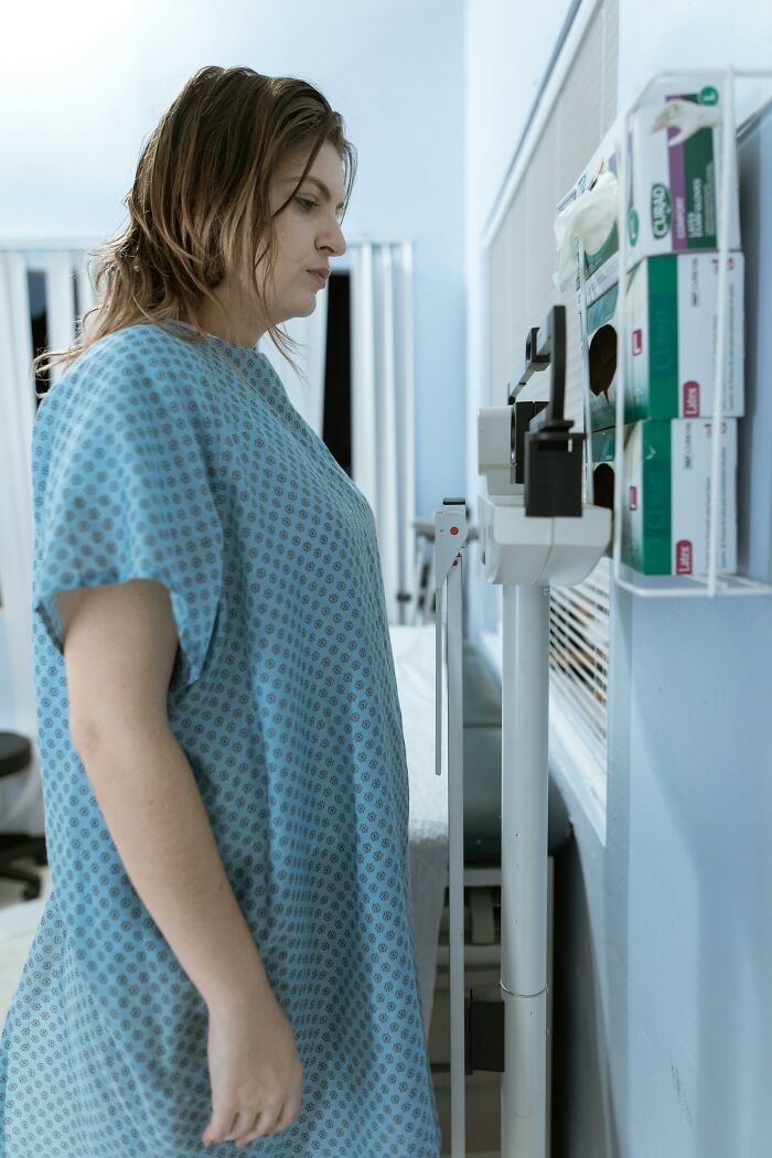 Woman in hospital gown standing on scale in medical setting
