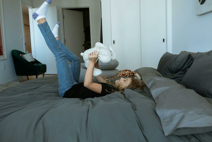 Girl playing with teddy bear on bed with weird confessions vibe