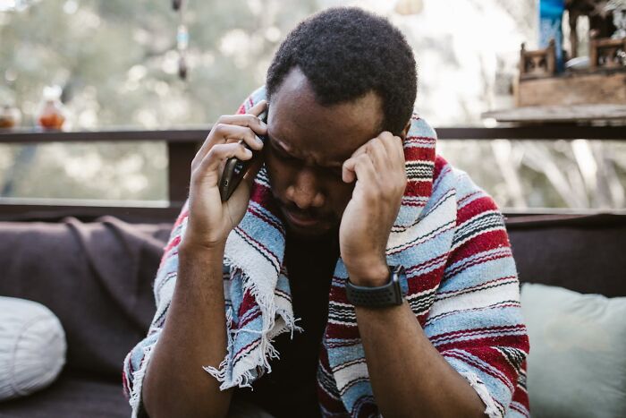 Stressed man talking on phone wrapped in blanket