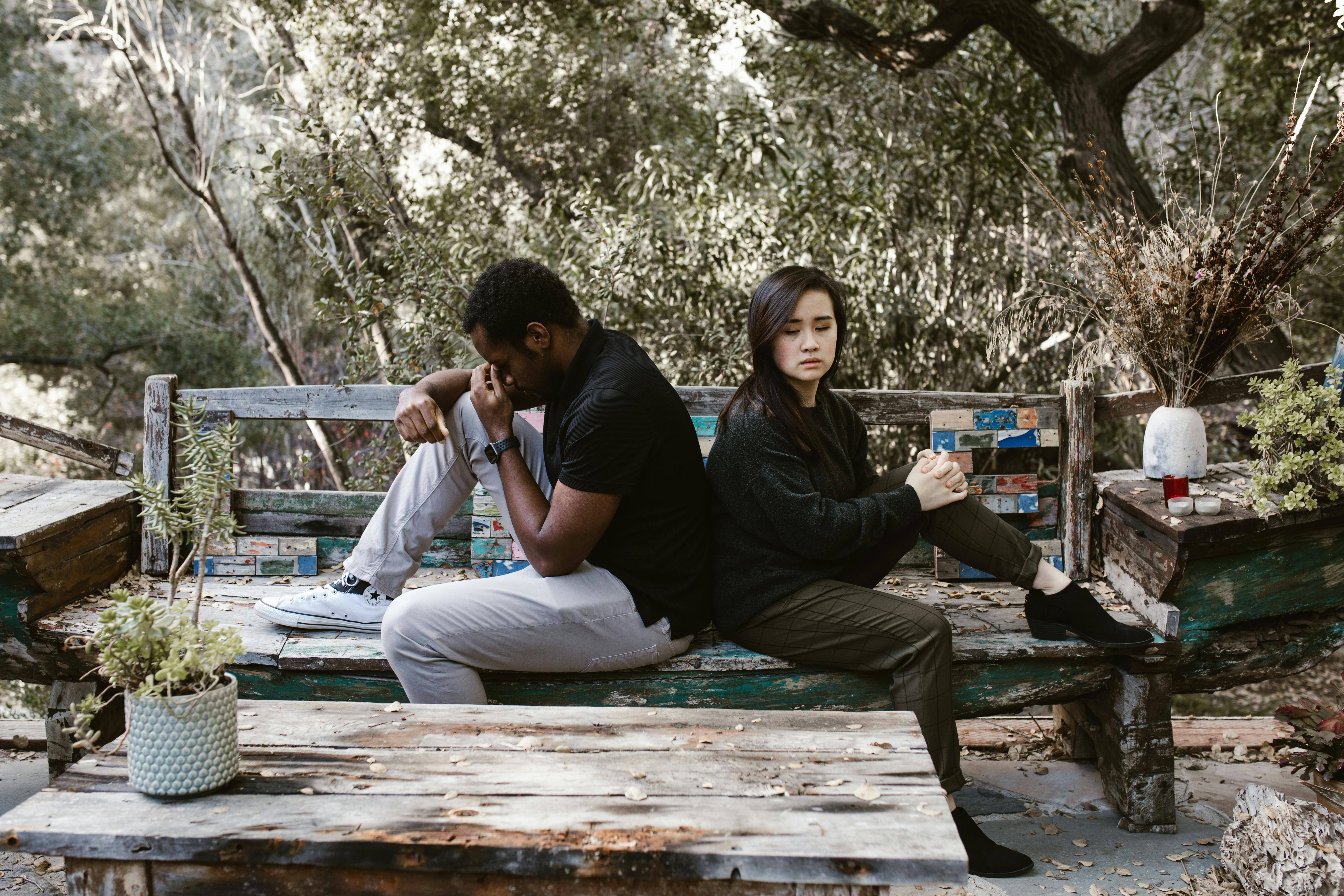 Couple sitting back to back looking upset outdoors on wooden bench in tense moment