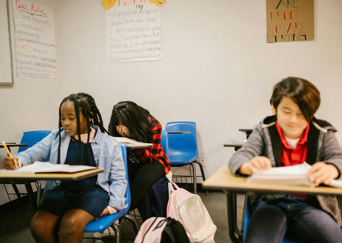 Criança escondendo o rosto na sala de aula com outros alunos Criança escondendo o rosto na sala de aula com outros alunos