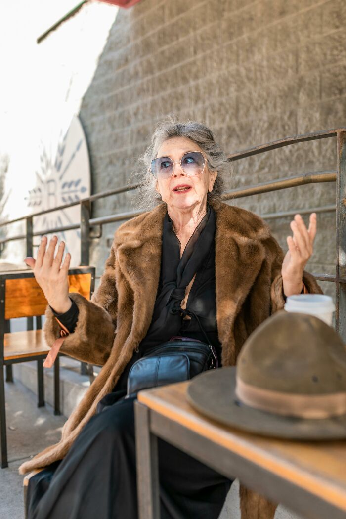 Elderly woman wearing fur coat and sunglasses enjoying outdoor cafe conversation