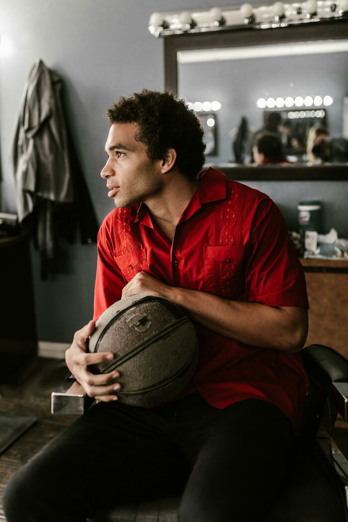 Man in red shirt holding a basketball while looking away thoughtfully