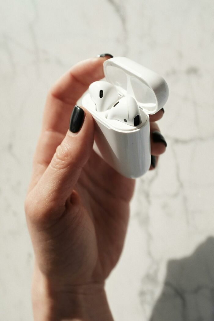 A hand with black nail polish holds an open white AirPods case, showcasing the earbuds. Perhaps a glitch in the matrix?