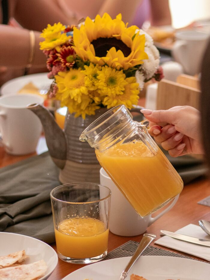 Pouring orange juice at a breakfast table with flowers and plates