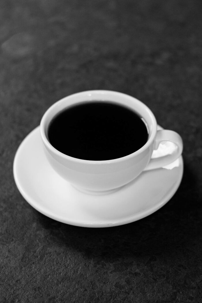 White cup filled with black coffee on white saucer on dark surface
