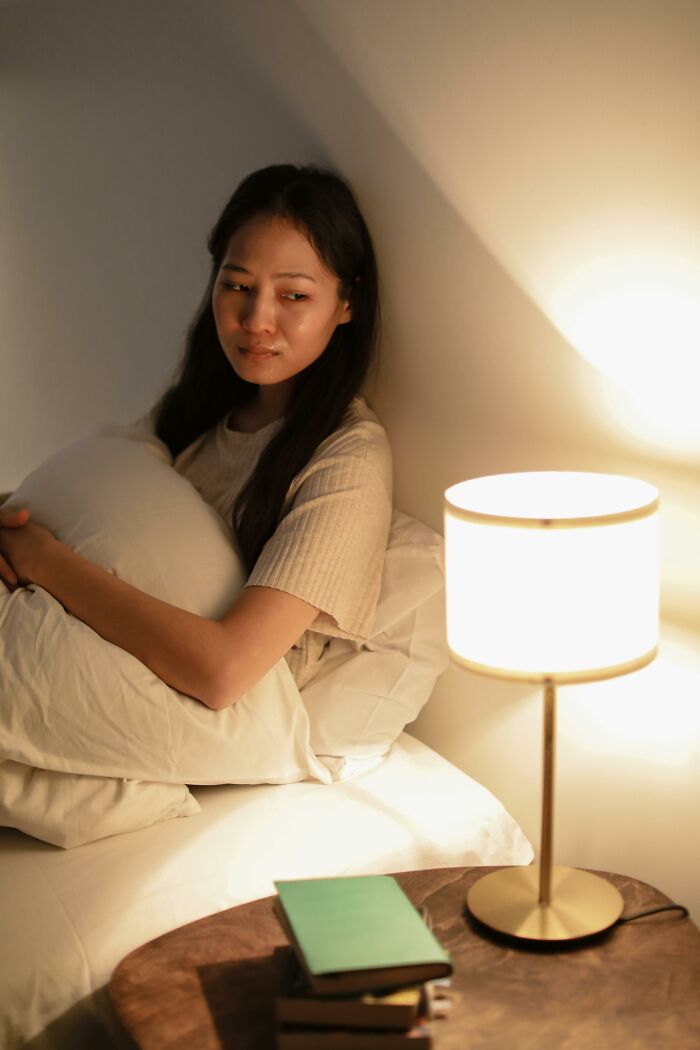 Woman in bed looking upset under warm lamp light weird confessions