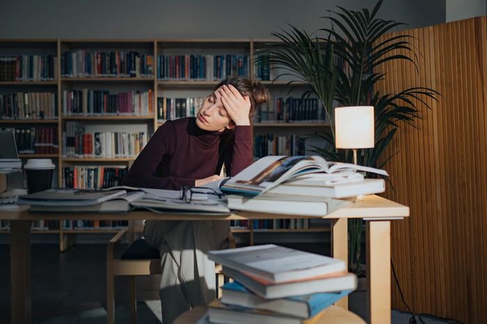 Tired woman studying surrounded by books, depicting laziness saving from disaster