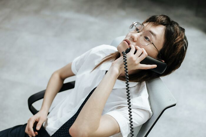 Gen Z person in glasses, leaning back in a chair, talking on a corded phone, showing one thing Gen Z does.