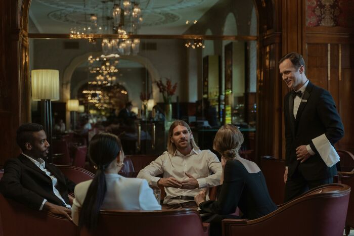 Well-dressed people conversing with waiter in luxury restaurant scene