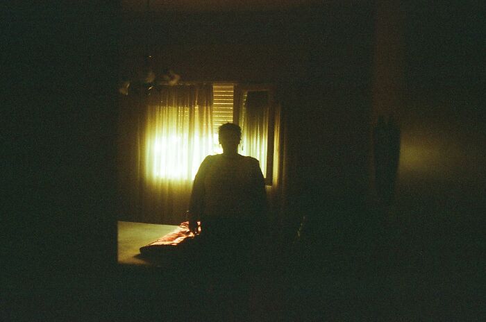 Silhouette of person in dimly lit room with window light, neighbors from hell vibes