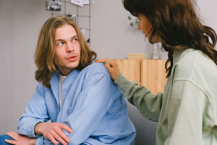 A woman comforts a man with long hair, discussing very creepy things. She gently touches his shoulder as he listens.