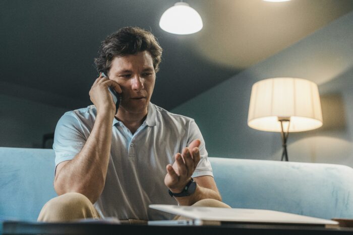 Man sitting on couch talking on phone discussing job and HR issues Man sitting on couch talking on phone discussing job and HR issues