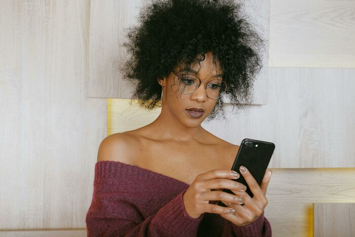 A woman with curly hair and glasses looks intently at her phone, reflecting on discovering a cheating partner.