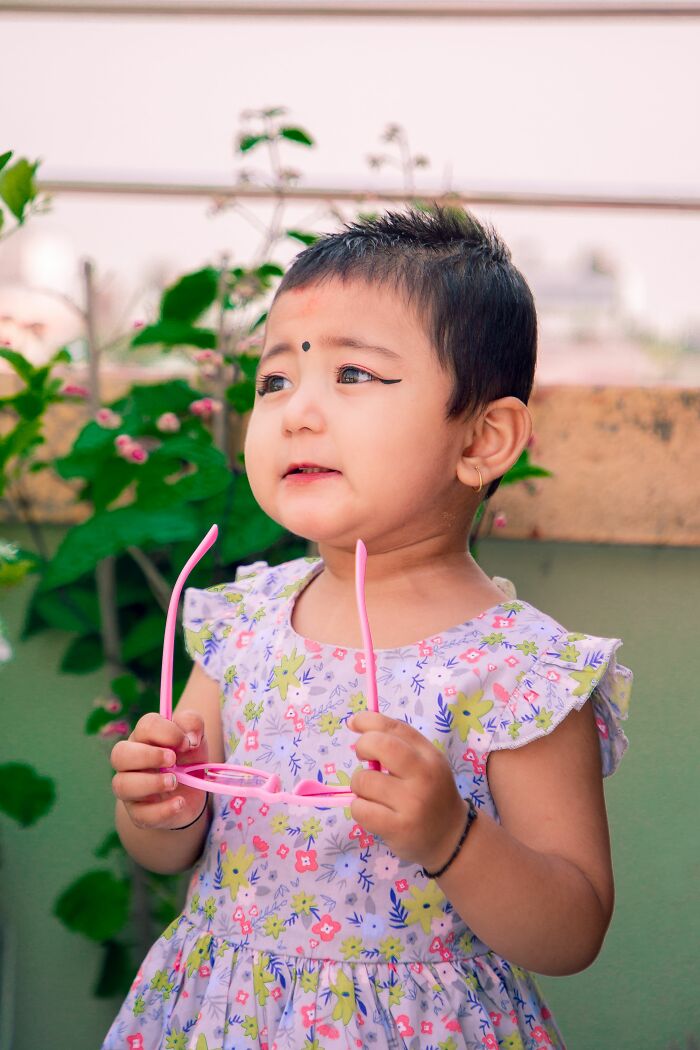 Toddler holding pink glasses outdoors wearing floral dress