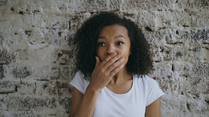 Woman surprised covering mouth expressing shock indoors
