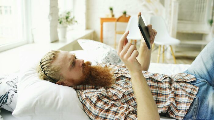 Man lying on bed using smartphone, representing long term partners relaxing