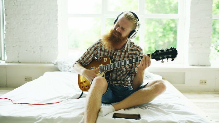 Man playing electric guitar loudly with headphones annoyed neighbors