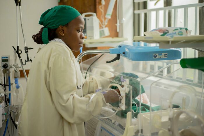 A nurse in a green scrub cap and light uniform tends to a baby in an incubator, representing a hard case or impossible situation overcome.