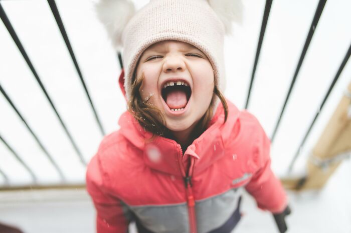 Child in winter hat and pink jacket yelling outdoors, neighbors from hell context