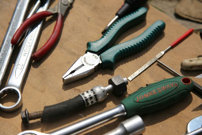 Various tools, including wrenches and pliers, on a wooden surface, showing how habits can save you money.