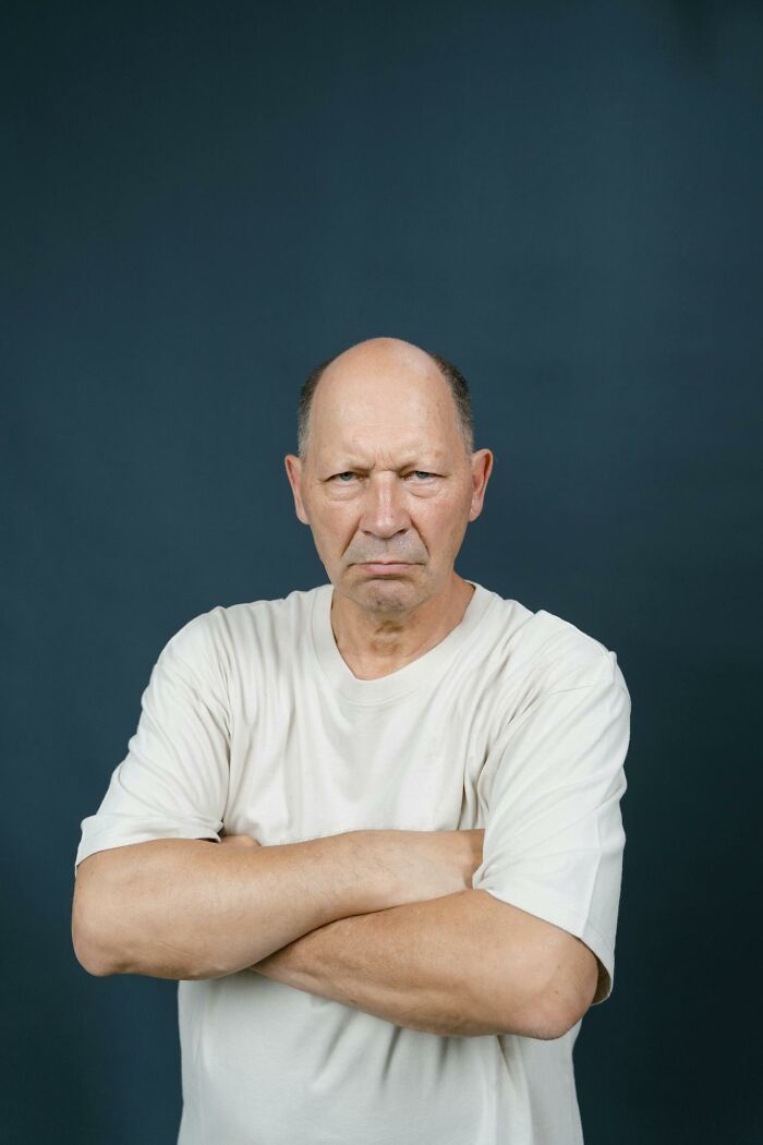 A man with a serious expression and crossed arms, wearing a light t-shirt, depicting deeply immoral things.