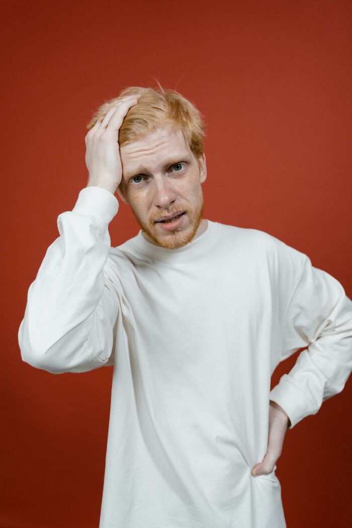 Confused man in white shirt touching his head against red background