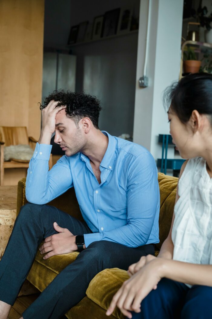 Man in blue shirt looking frustrated while sitting on a couch with a woman