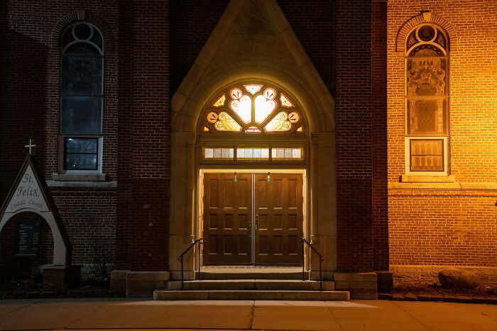 Front entrance of a cult church building at night with illuminated stained glass