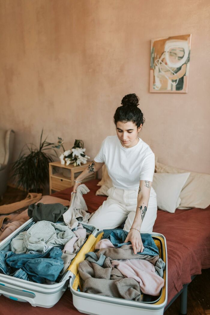 A woman kneeling on a bed, packing clothes into an open suitcase, experiencing glitches in the matrix.