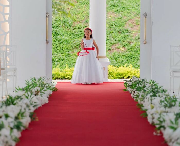 Flower girl in white dress standing on red carpet at wedding venue wedding photography