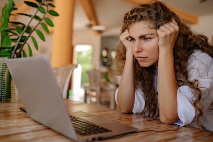 A young Gen Z woman with curly hair looking intently at her laptop, seemingly confused or focused.