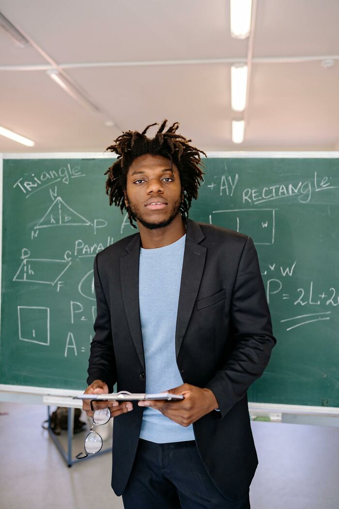 Teacher explaining geometry concepts with formulas on chalkboard behind him