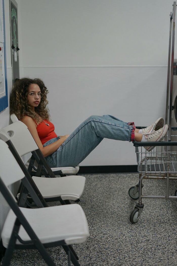 Young woman sitting relaxed in laundromat with feet on cart