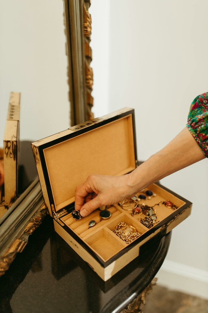 A person's hand selecting a ring from an open jewelry box with many accessories, questioning reality.