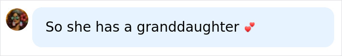 A chat bubble with an avatar showing a woman with dark hair, glasses, and a flower. The message says: So she has a granddaughter ❤️. Woman has child update.