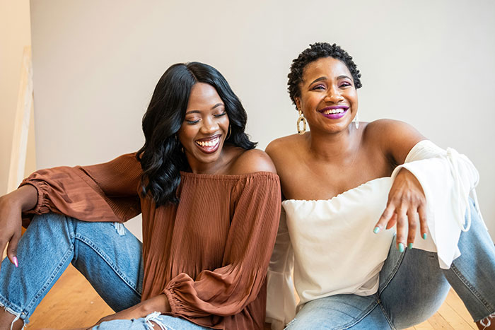 Two smiling sisters sitting together indoors showing a close bond