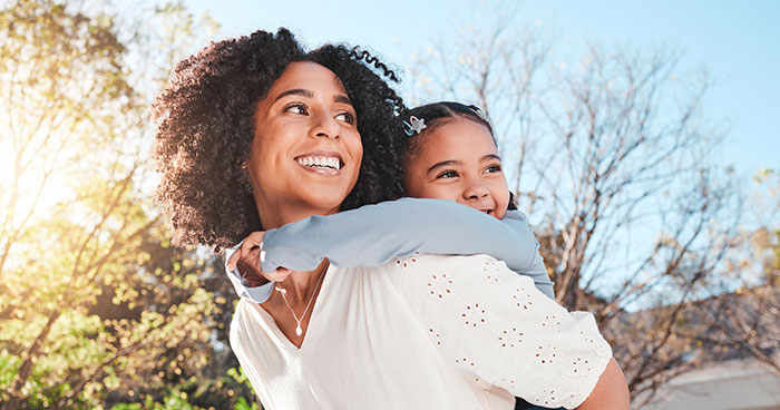 Young woman giving piggyback ride to happy child outdoors rent and childcare help