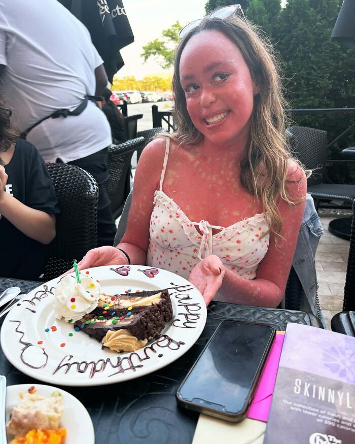 Um adolescente com um raro problema de pele sorri, segurando uma fatia de bolo de aniversário. Ela está em um restaurante ao ar livre.